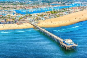 Un muelle que se adentra en el mar, con un barco amarrado al final, rodeado por una playa y un pueblo costero.
