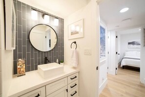 A modern bathroom with a large mirror, white sink, and tiled backsplash.