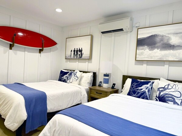 Habitación de hotel con dos camas, una tabla de surf roja y un cuadro con surfistas.