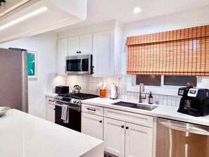 Una cocina moderna con armarios blancos, microondas, estufa y cafetera.