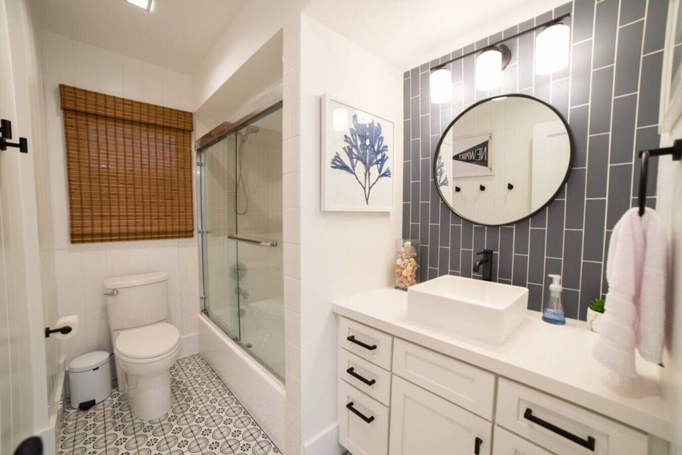 Un baño con inodoro, ducha con mampara de cristal, lavamanos con espejo y suelo de baldosas.