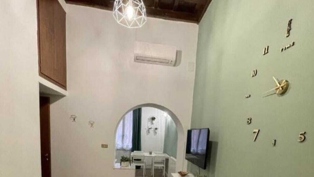 A room with a bed, a TV, a desk, and a mirror. There is a hallway leading to another room. - The ideal home for your stay in Rome  (Roma)