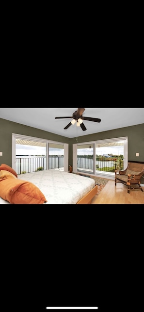Ein Schlafzimmer mit Bett, Deckenventilator, Stuhl und großen Fenstern.