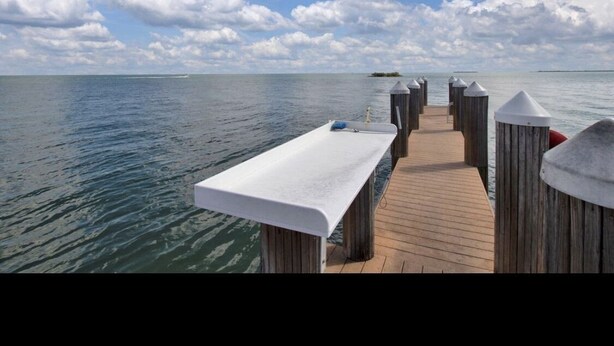 Un muelle de madera que conduce a una plataforma blanca con vistas al mar y al cielo.