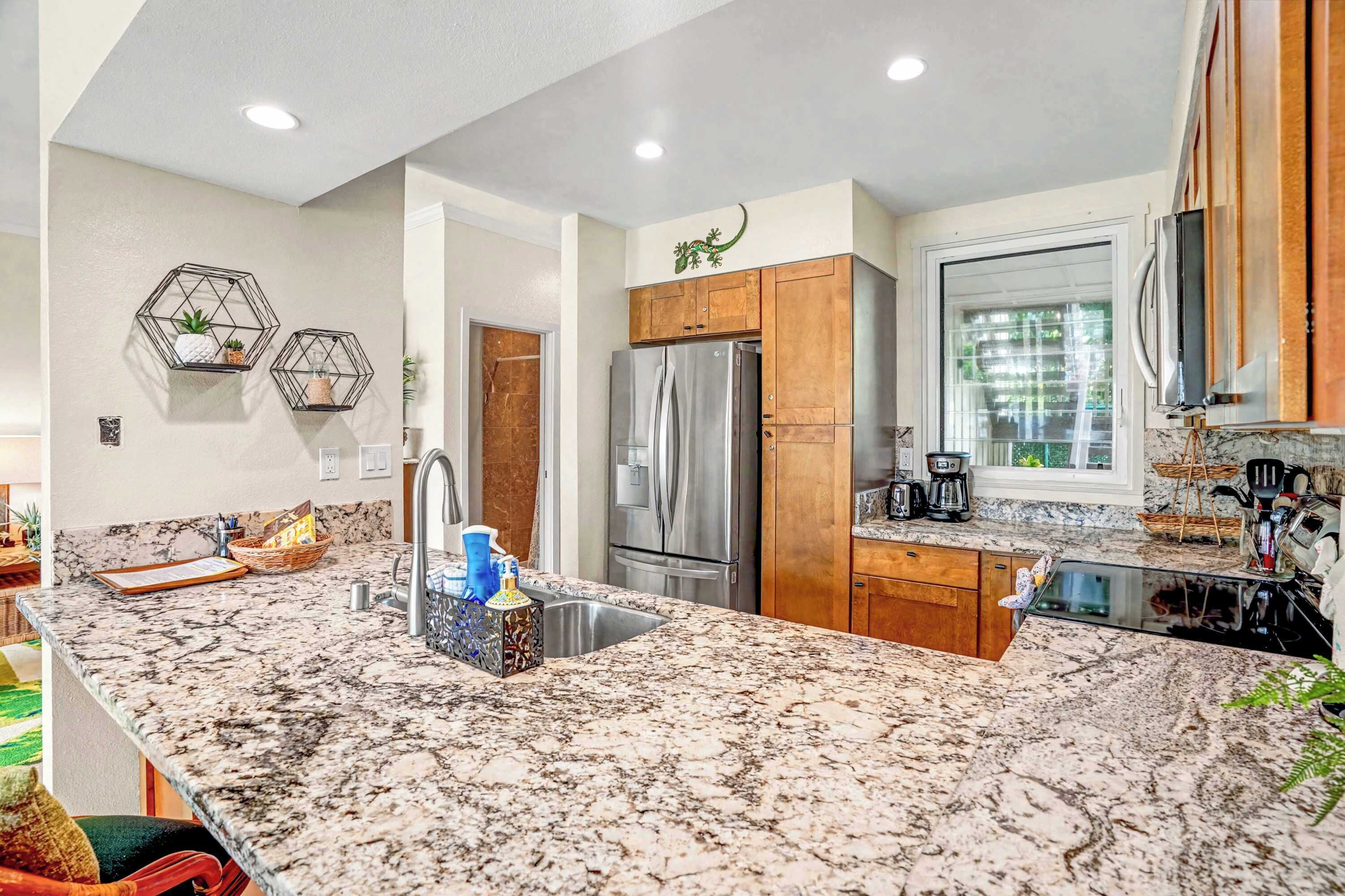 A modern kitchen with granite countertops, stainless steel appliances, wooden cabinets, and a window providing natural light.