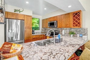 A modern kitchen with wooden cabinets, stainless steel appliances, a granite countertop, and a view of greenery outside.