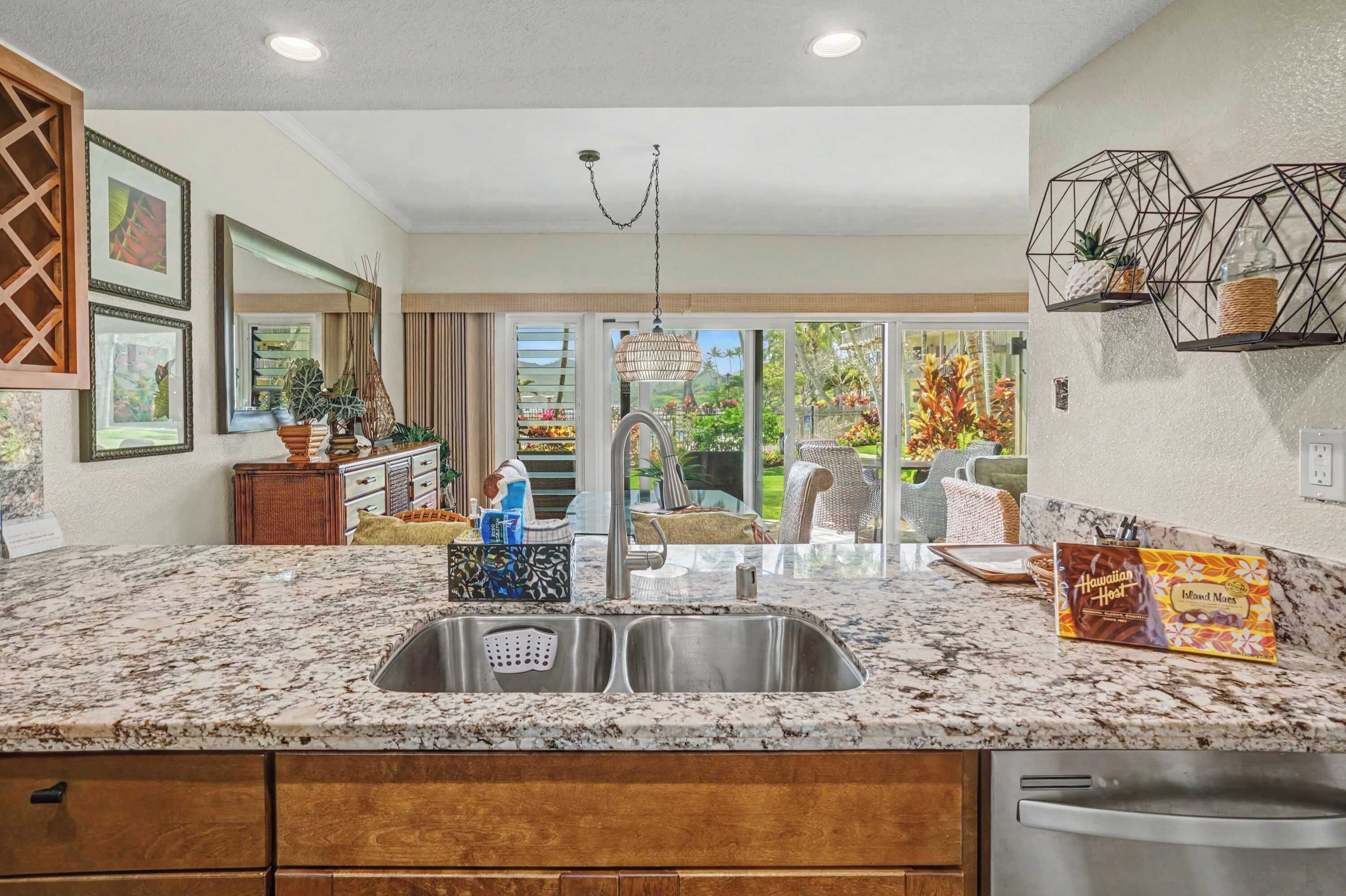 A kitchen with a granite countertop, stainless steel sink, and a view of a garden through large windows.