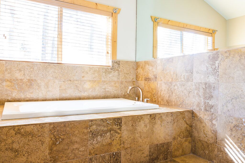 Un baño con una bañera grande, marcos de ventana de madera y paredes con azulejos.