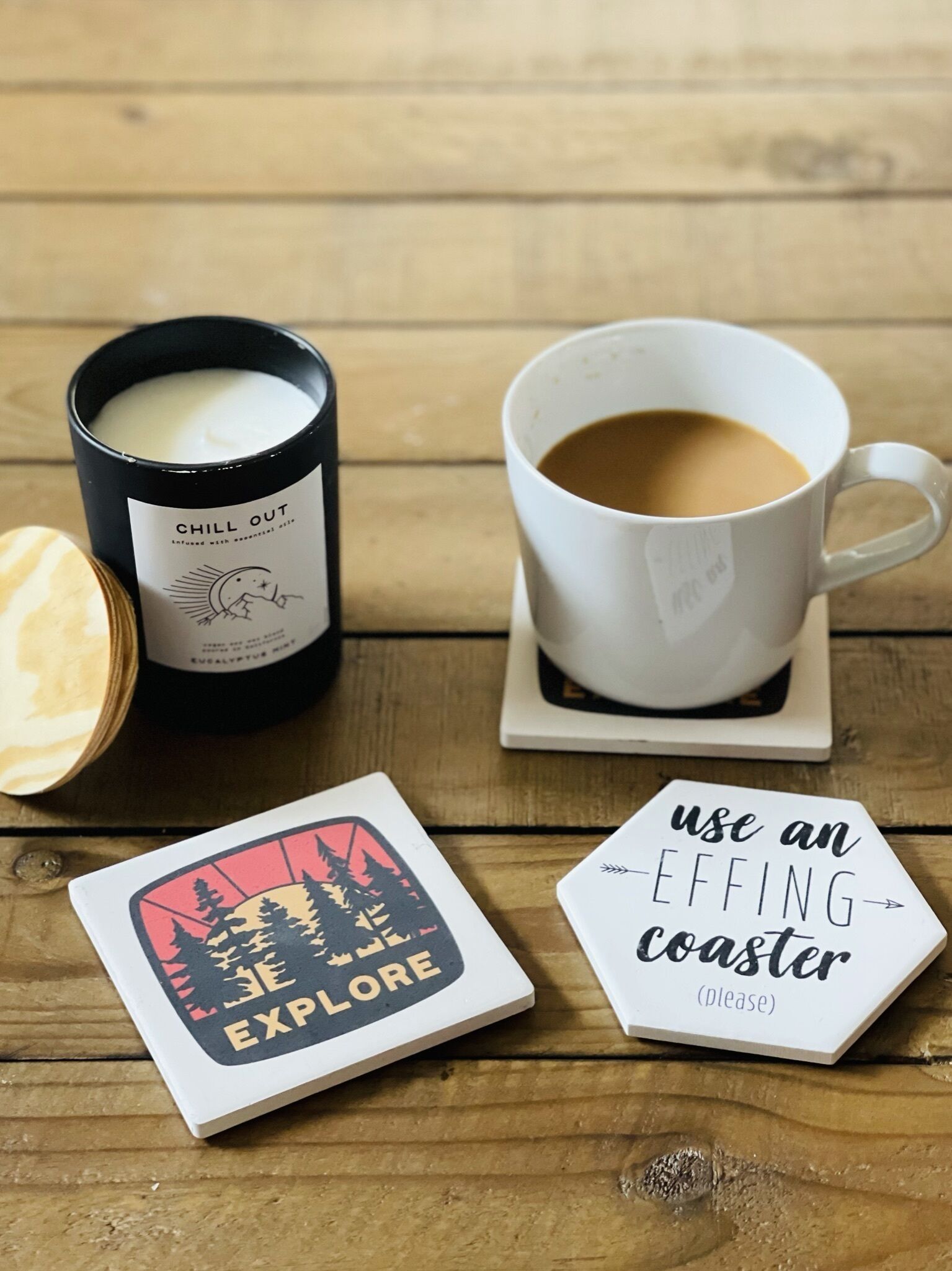 Een kaars, een kop koffie en twee onderzetters op een houten oppervlak.