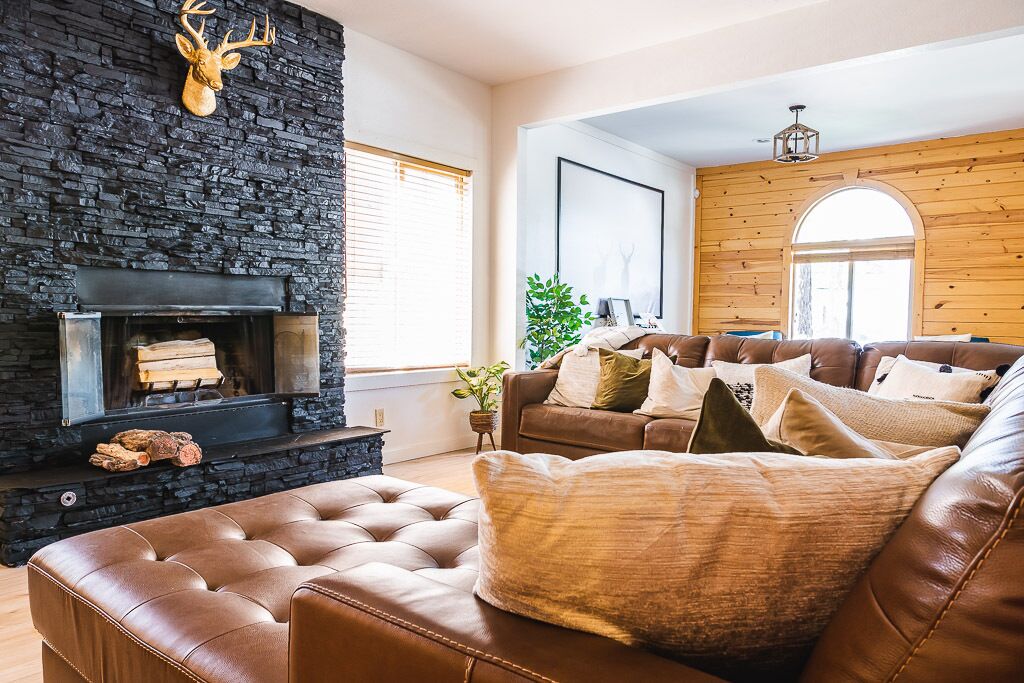 A living room with a stone fireplace, leather sofa, and wooden walls.