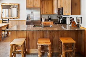 Una cocina con armarios de madera, un refrigerador de acero inoxidable, una cafetera y un bloque de cuchillos.
