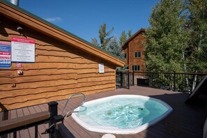 Eine Holzhütte mit Whirlpool auf einer Terrasse, umgeben von Bäumen.