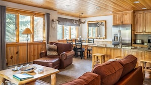 Ein gemütliches Blockhaus-Interieur mit Holzbalkendecke, einem Essbereich, einer Küche mit modernen Geräten und einem Kamin.