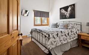 Ein Schlafzimmer mit Bett, Fenster mit Jalousien, einem Wand-Fernseher und einem Gemälde.