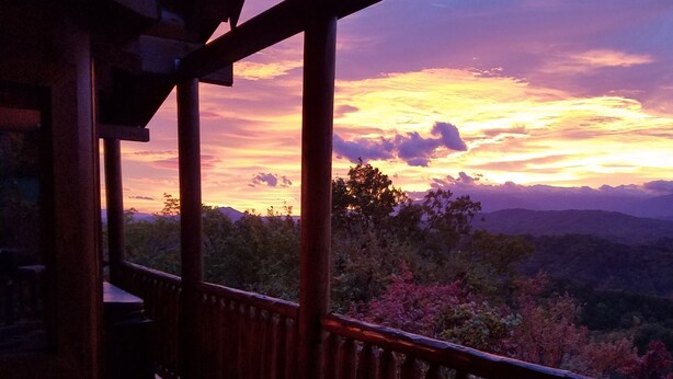 Um deck de madeira com guarda-corpo, com vista para uma paisagem montanhosa ao pôr do sol.