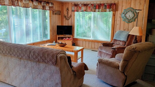 A cozy living room with a wooden floor, a brown sofa, a recliner, a wooden coffee table, and a television on a stand. - Private Up North getaway - short walk to lake (Spruce)