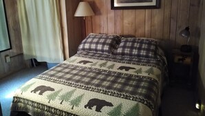 A wooden-paneled room with a bed, a framed picture on the wall, a lamp, and a window with curtains. - Private Up North getaway - short walk to lake (Spruce)