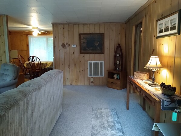 A cozy room with wooden paneling, a ceiling fan, a framed picture, a lamp, and a small table with a basket. - Private Up North getaway - short walk to lake (Spruce)