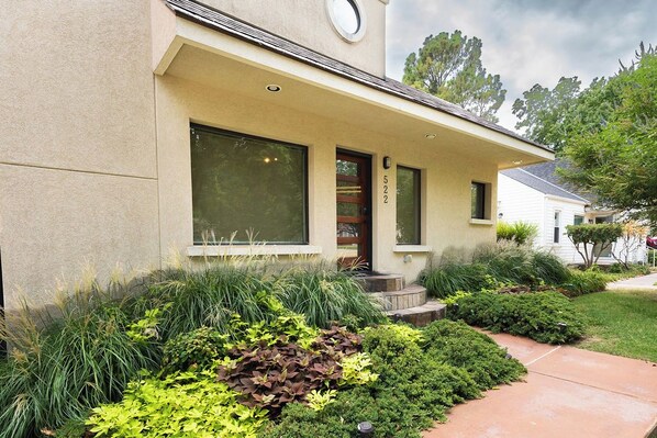 A residential building with a beige exterior, large windows, and a well-maintained garden with various plants.