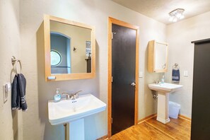A bathroom with a white sink, a mirror, a door, and a small pedestal sink.