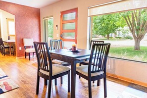 A dining area with a wooden table and chairs, a door with frosted glass panels, and a view of a tree and lawn outside.