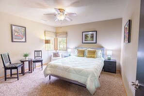 A bedroom with a bed, a ceiling fan, a window, a chair, a small table, and a nightstand.