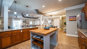 A spacious kitchen with wooden cabinets, a central island, pendant lighting, and a view into the dining area.