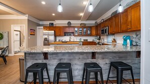 A modern kitchen with granite countertops, wooden cabinets, and a central island with bar stools.