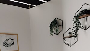 Un dormitorio ordenado con cama, mesita de noche, lámpara y decoraciones geométricas en la pared.