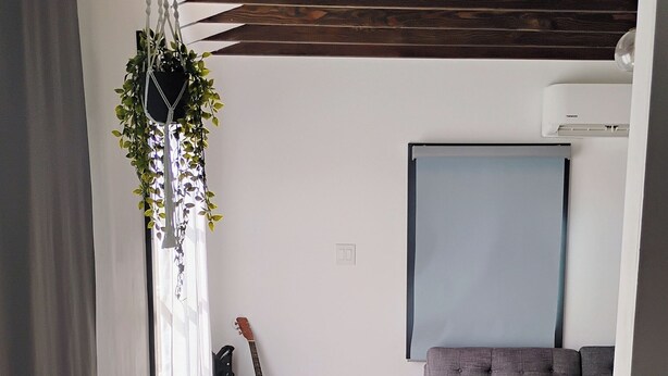 Un salón moderno con suelo de madera, un sofá gris, una mesita, una guitarra y una planta decorativa.