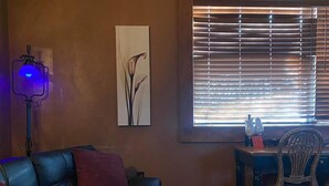 Ein Wohnzimmer mit einer schwarzen Ledersofa, einem Holztisch, einem bunten Teppich, einem Bild an der Wand und einem Fenster mit Jalousien.
