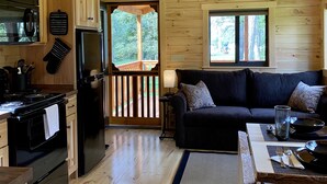 Interior de una cabaña de madera con cocina, comedor y balcón con vistas a árboles.