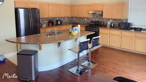 Eine moderne Küche mit Granit Arbeitsplatten, Edelstahlgeräten, Holzschränken und einer integrierten Kücheninsel mit Barhocker.