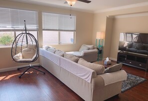 Una sala de estar con un sillón colgante, un conjunto de sofá, un televisor y una lámpara de pie.