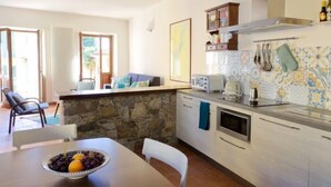 A kitchen with a stone wall, white cabinets, a microwave, and a toaster. There is a dining table with a bowl of fruit. - Canton Balin by Interhome (Meina)