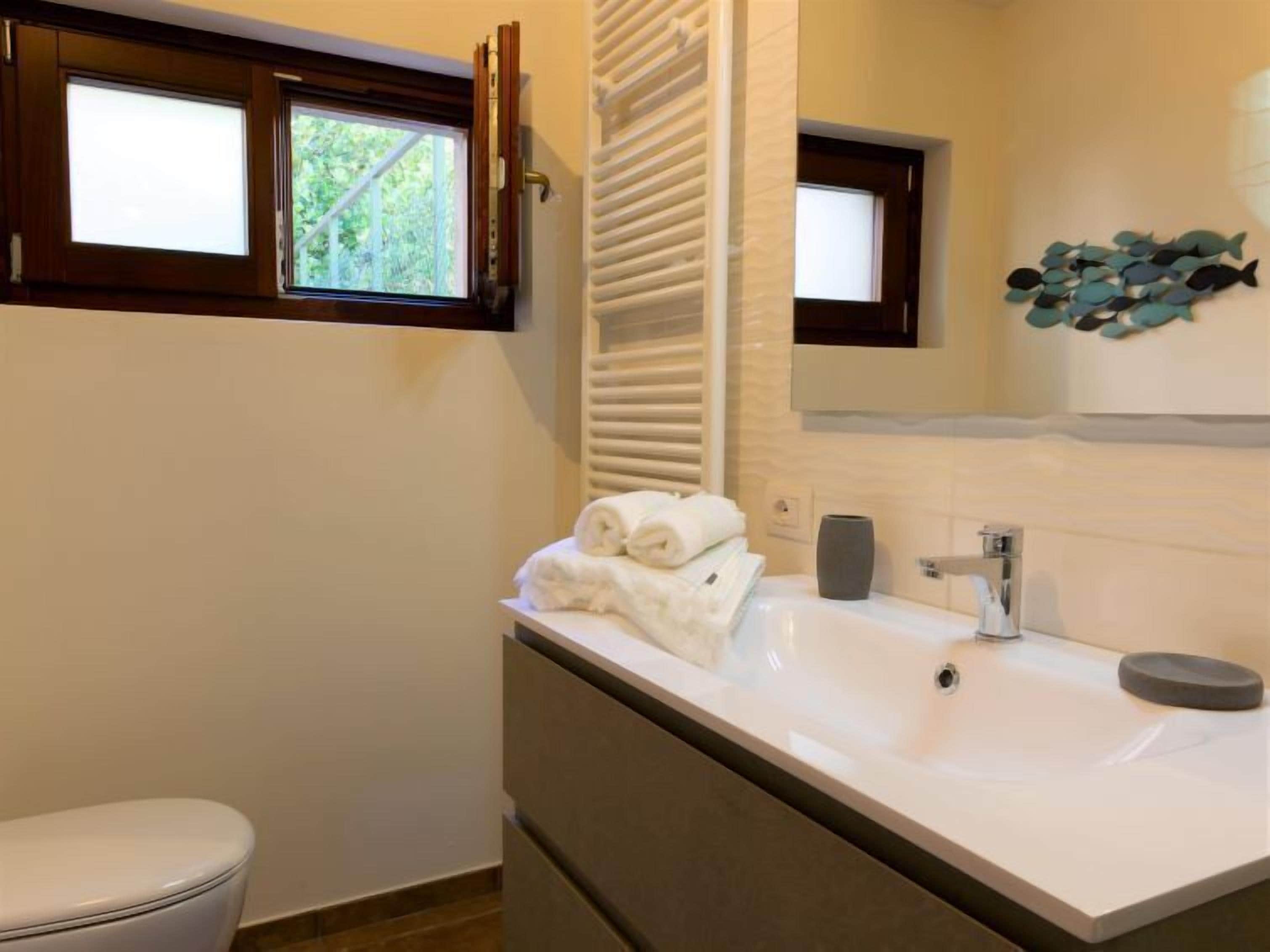A bathroom with a white sink, a towel rack with folded towels, a mirror, and a window with blinds.