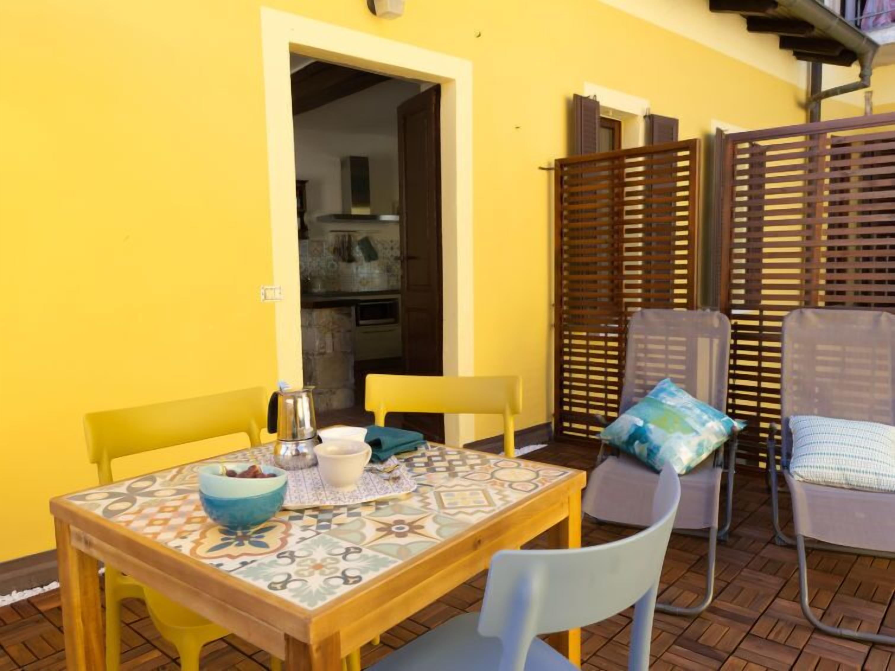 An outdoor patio with a tiled table, yellow chairs, and a wooden partition.