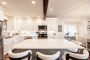 A modern kitchen with white cabinetry, a large island with bar stools, a built-in microwave, and a stove.