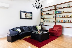 A modern living room with a black leather sofa, a red armchair, a black coffee table, a red rug, a bookshelf, and a chandelier.