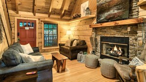 Ein gemütliches Blockhaus-Interieur mit Kamin, Holzwänden, einer Wand aus Naturstein und einer komfortablen Sitzecke.