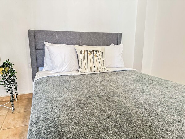 A bed with a grey headboard, white pillows, and a grey textured bedspread. - Boulevard 107 (Mayagüez)