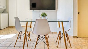 A modern kitchen with a built-in oven, a dining area with a glass table and white chairs, and a flat-screen TV mounted on the wall. - Boulevard 107 (Mayagüez)
