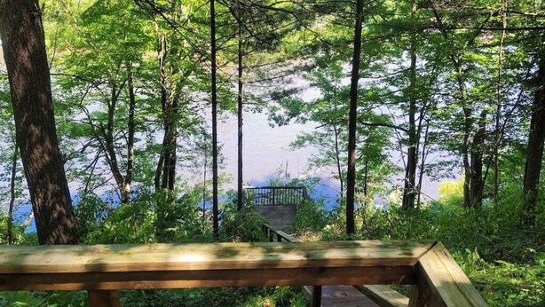 Une terrasse en bois donnant sur un lac, avec une rambarde en métal et un escalier menant à un quai.