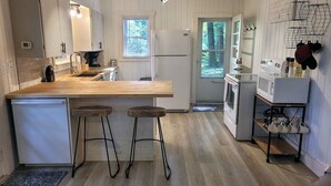 Une cuisine compacte dotée d’un plan de travail en bois, de deux tabourets, d  ’un réfrigérateur, d’un four à micro-ondes et d’un évier.