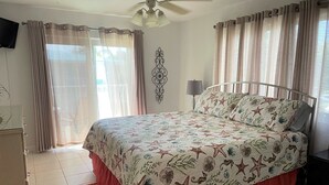 Une chambre à coucher avec un lit, des rideaux, un ventilateur de plafond, une télévision et un tapis rouge.