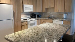 Une cuisine avec des meubles de rangement en bois, un réfrigérateur blanc, un four à micro-ondes, une cuisinière et un lave-vaisselle.