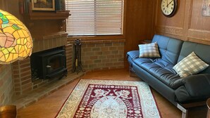 Una sala de estar acogedora con chimenea, un sofá de cuero azul, un tapete estampado y un reloj de pared grande.