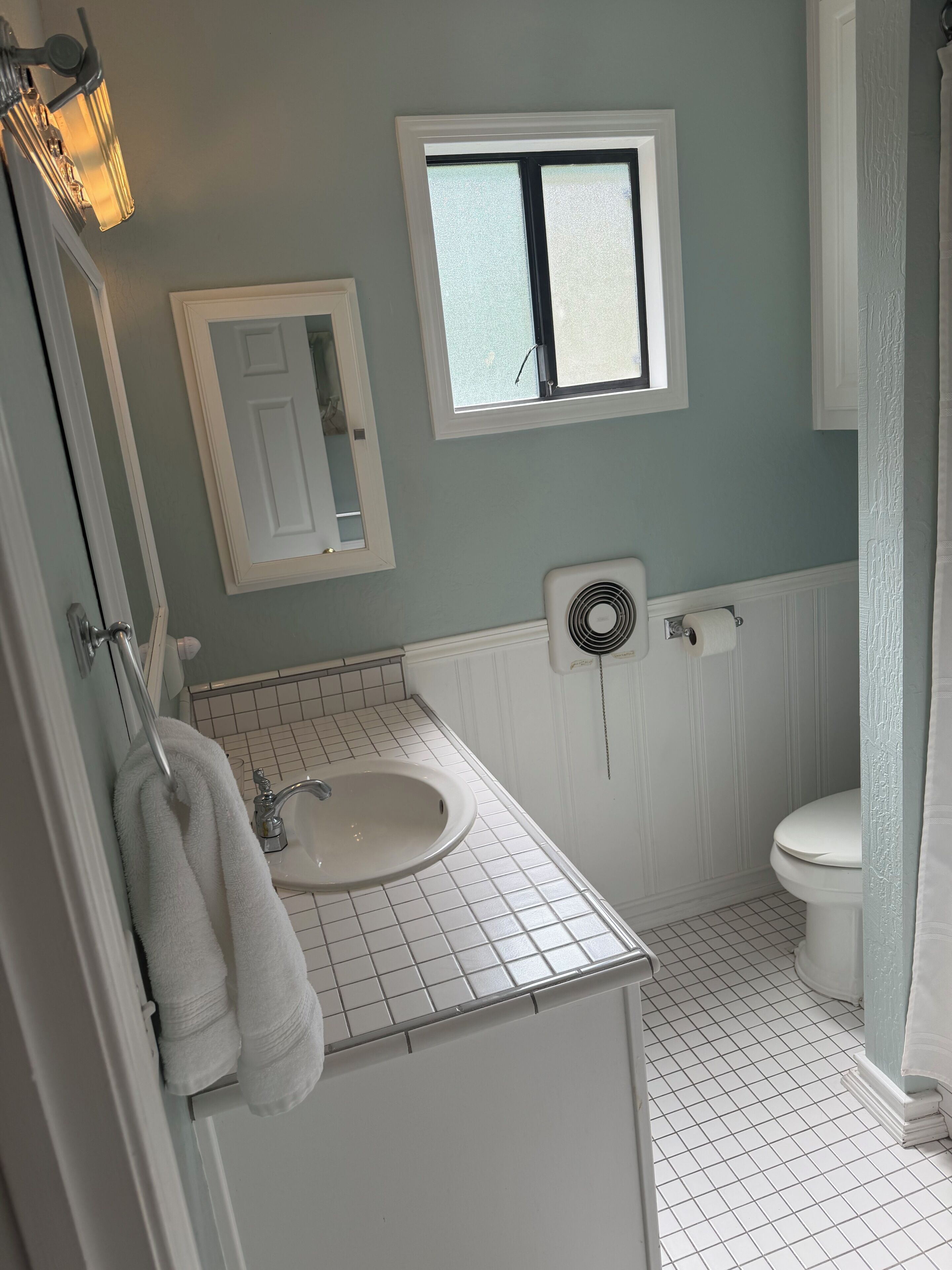Un baño con un lavamanos blanco, un espejo, una ventana, un inodoro y un perchero para toallas.