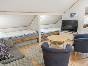 Et lille værelse med to køjesenge, et fjernsyn, et rundt bord og en sofa.