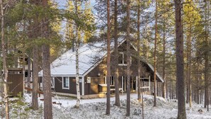 Une cabane entourée de grands arbres dans une forêt enneigée.